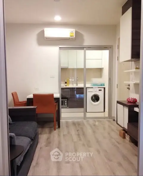 Modern living room with open kitchen and washing machine, featuring sleek design and wooden flooring.