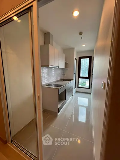 Modern kitchen with sleek cabinetry and city view window in high-rise apartment.