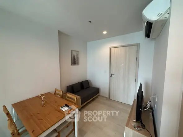 Modern living room with wooden dining table, cozy sofa, and wall-mounted TV in a compact apartment.