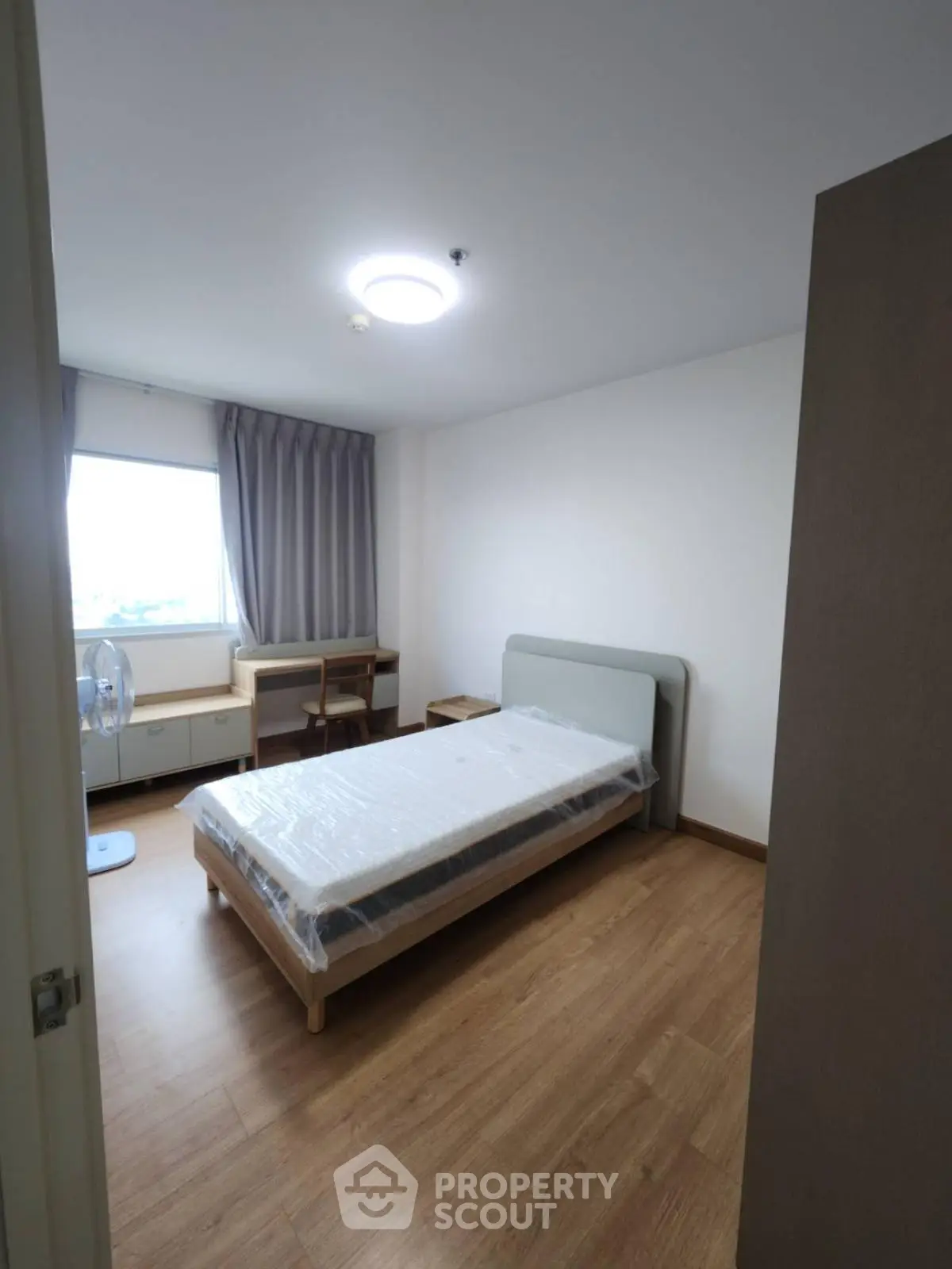 Cozy bedroom with wooden flooring and natural light from large window.