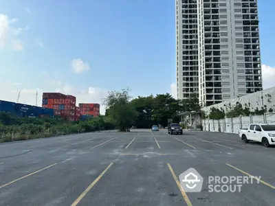 Spacious outdoor parking area adjacent to a modern high-rise residential building, offering ample parking spaces and easy access to urban amenities.