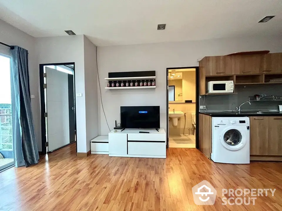 Modern apartment interior with wooden flooring, open kitchen, and washing machine.