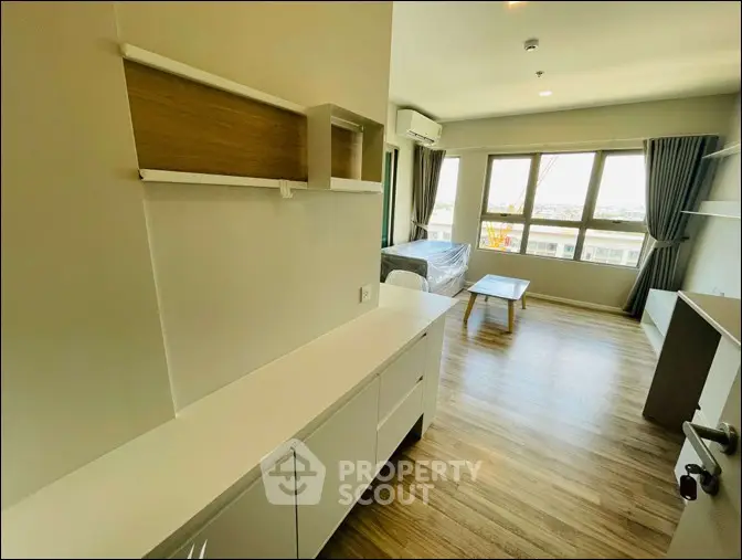 Modern living room with wooden flooring and large windows offering natural light.