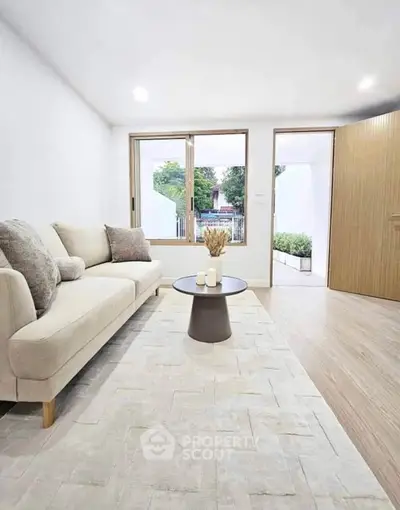 Modern living room with cozy beige sofa and stylish coffee table, featuring large windows and wooden flooring.