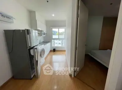 Modern apartment interior with kitchen and bedroom, featuring wooden flooring and natural light.