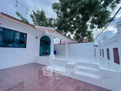 Charming white exterior home with spacious tiled patio and lush greenery.