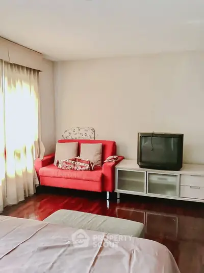 Cozy bedroom with vintage TV and vibrant red sofa, perfect for relaxation.