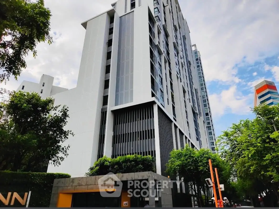 Modern high-rise building with sleek design and lush greenery in urban setting.