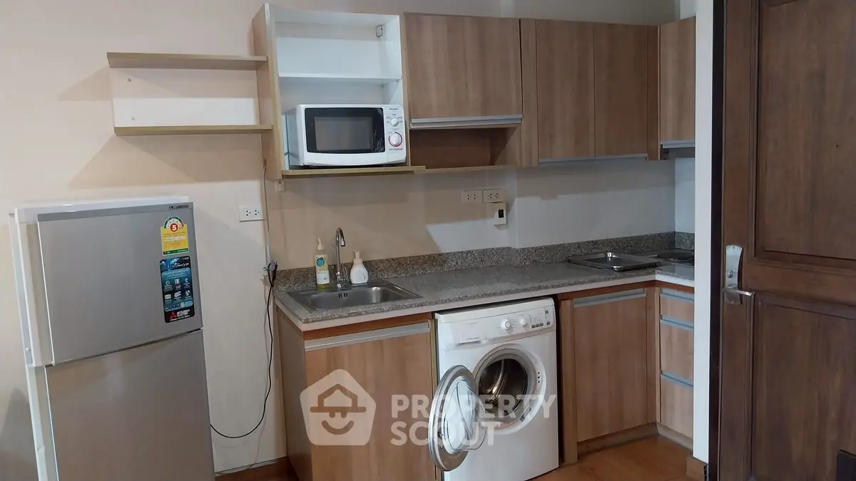 Modern kitchen with wooden cabinets, microwave, fridge, and washing machine in compact layout.