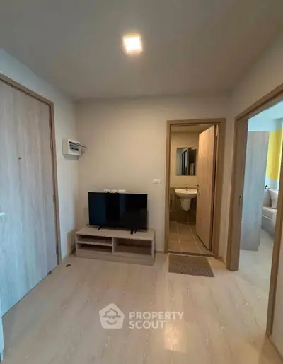 Modern apartment interior with TV, light wood flooring, and bathroom access.