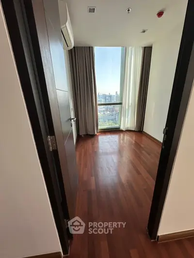 Spacious bedroom with wooden flooring and city view through large window