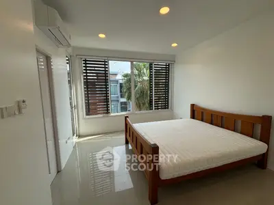 Spacious bedroom with large window and wooden bed frame, offering natural light and modern design.