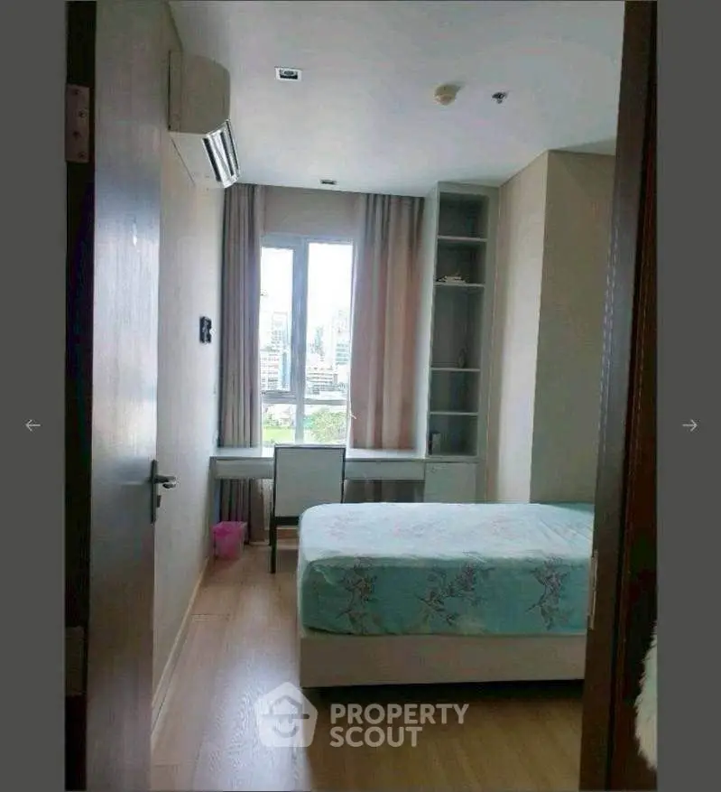 Cozy bedroom with city view, featuring a bed, desk, and built-in shelves, perfect for urban living.