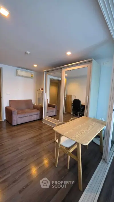 Modern living room with wooden flooring, mirrored wardrobe, and cozy seating area.