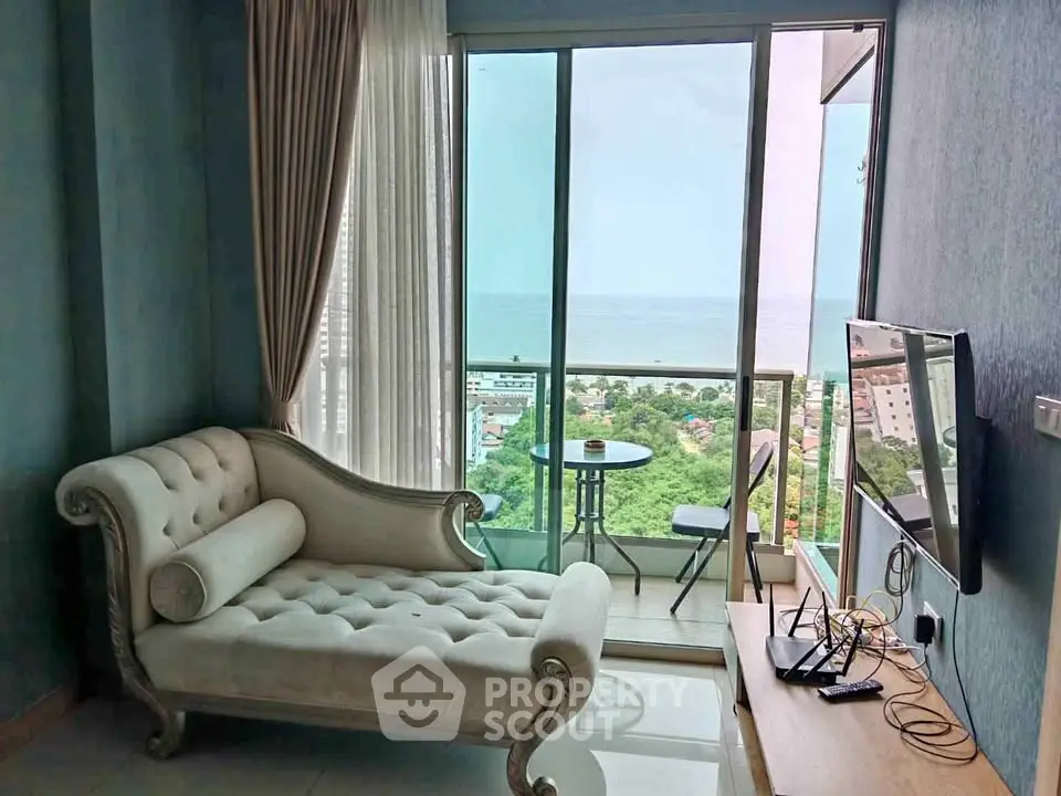 Luxurious living room with stunning ocean view from high-rise balcony, featuring elegant chaise lounge and modern TV setup.