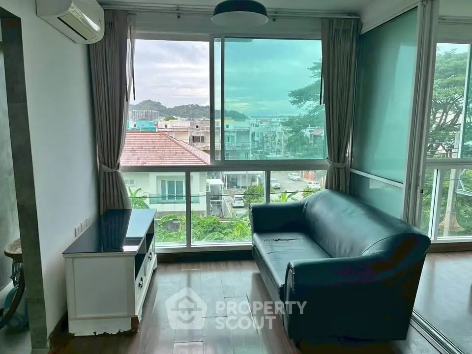 Cozy living room with large windows offering a scenic view, featuring a black sofa and wooden flooring.
