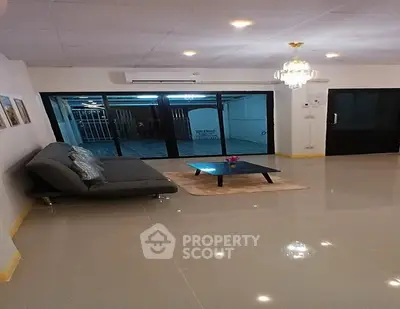 Spacious living room with modern sofa and chandelier, featuring large sliding glass doors.