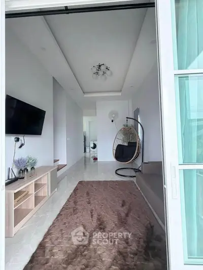 Modern living room with stylish decor and hanging chair, featuring a sleek TV setup and plush carpet.