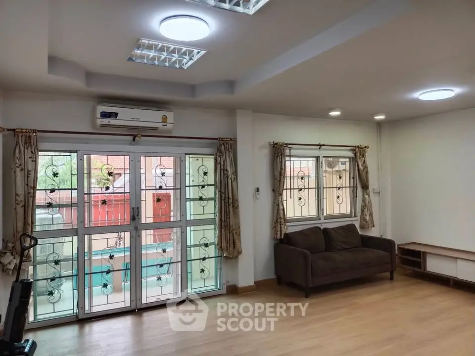 Spacious living room with large windows and modern lighting in a cozy apartment.