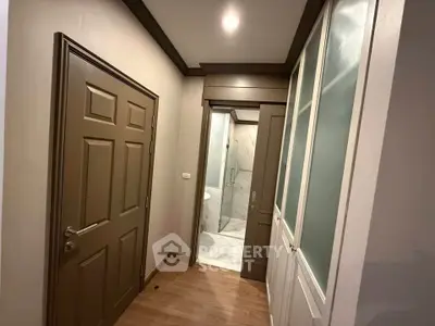 Modern hallway with wooden flooring leading to a sleek bathroom with glass shower.