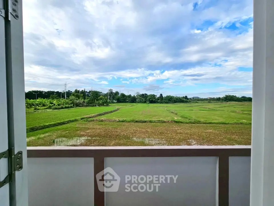 Stunning view from balcony overlooking lush green fields and blue sky.