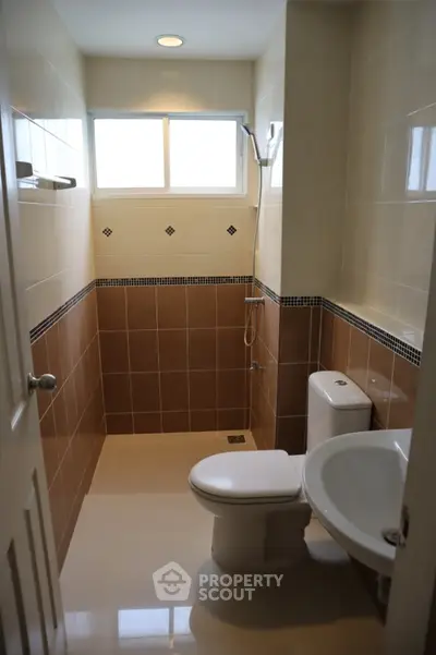 Modern bathroom with sleek tile design and natural light from a frosted window, featuring a shower and toilet.