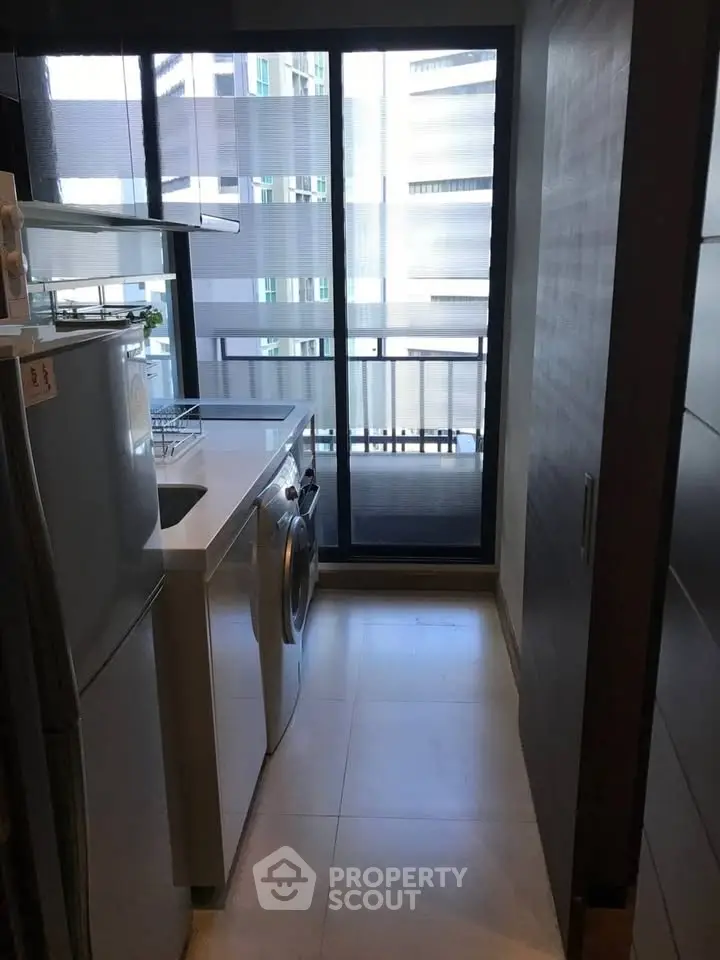 Modern kitchen with washing machine and balcony view in urban apartment.