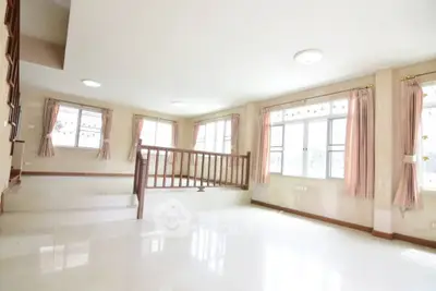 Spacious sunlit living room with large windows and elegant curtains in a modern home.