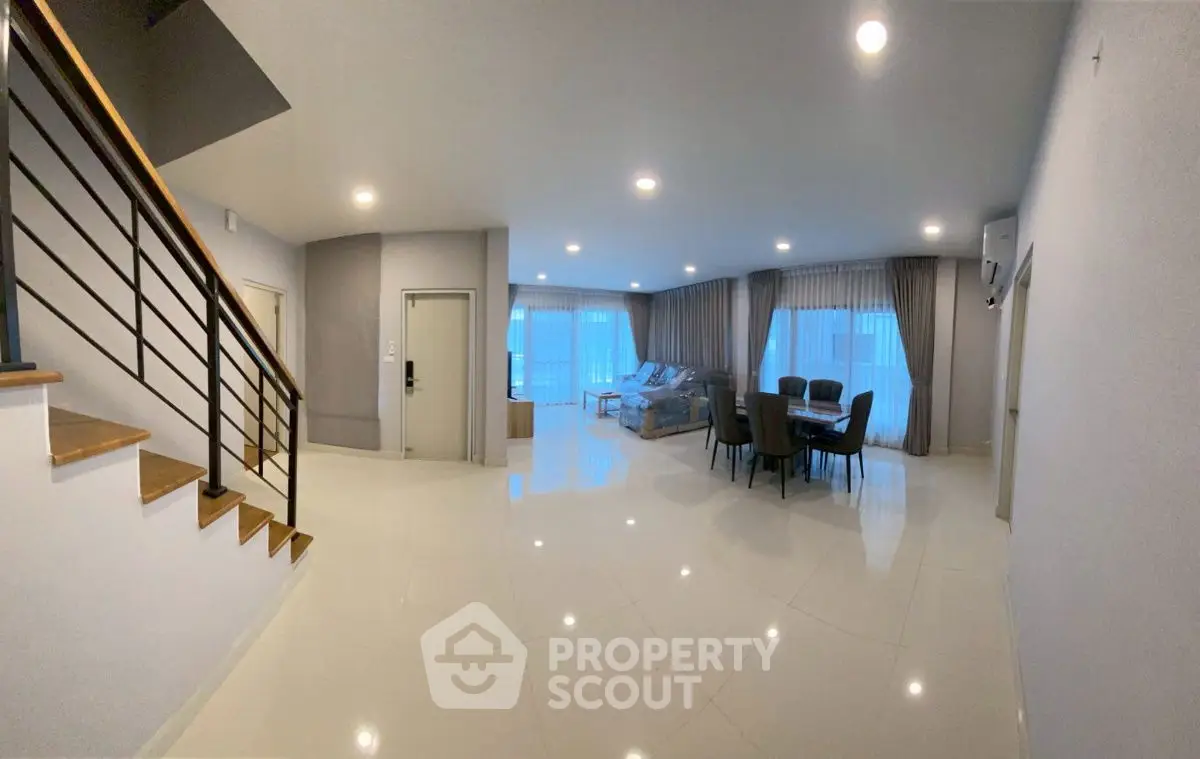 Spacious modern living room with elegant dining area and staircase, featuring sleek design and ample natural light.