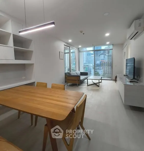 Modern living room with dining area and city view, featuring sleek furniture and ample natural light.