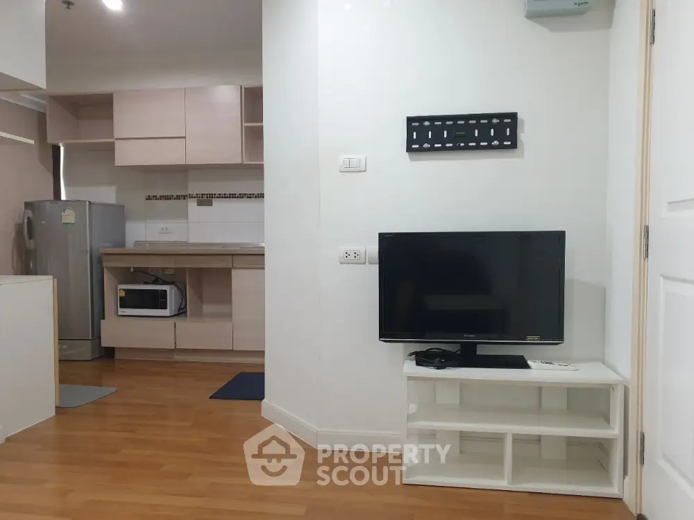 Modern apartment interior with kitchen and living area featuring wooden flooring and mounted TV.