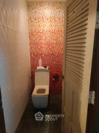 Compact bathroom with vibrant mosaic tile wall and modern toilet design.