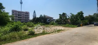 Vacant land plot in a residential area with nearby buildings and clear sky.