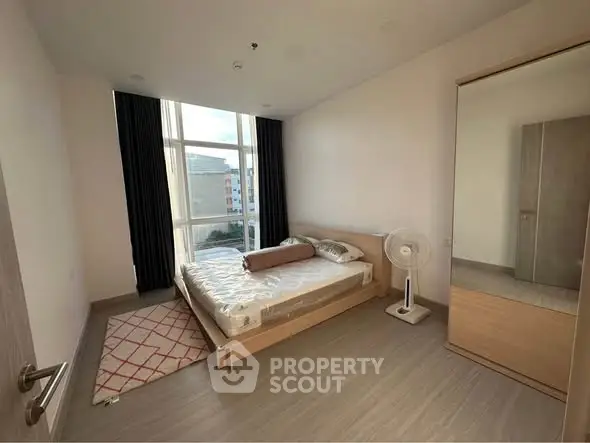 Spacious bedroom with large window and modern furnishings in a high-rise apartment.