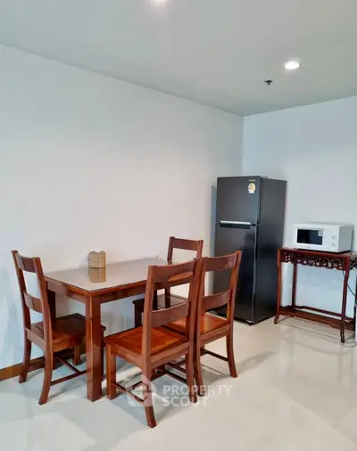 Modern dining area with wooden table, chairs, fridge, and microwave in a sleek kitchen corner.