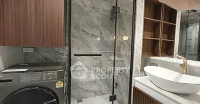 Modern bathroom with glass shower, washing machine, and stylish sink in luxury apartment.