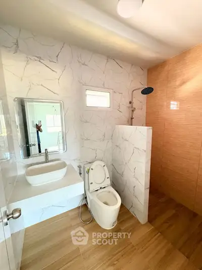 Modern bathroom with marble walls and wooden flooring, featuring a sleek shower and stylish sink.