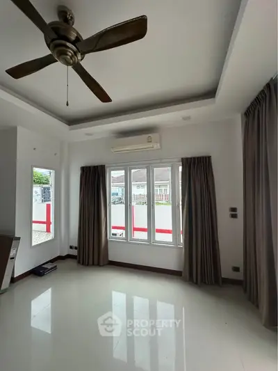 Spacious room with ceiling fan and large windows offering ample natural light.