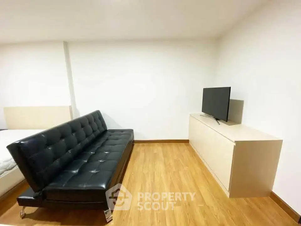 Modern living room with sleek black sofa and flat-screen TV on wooden floor.