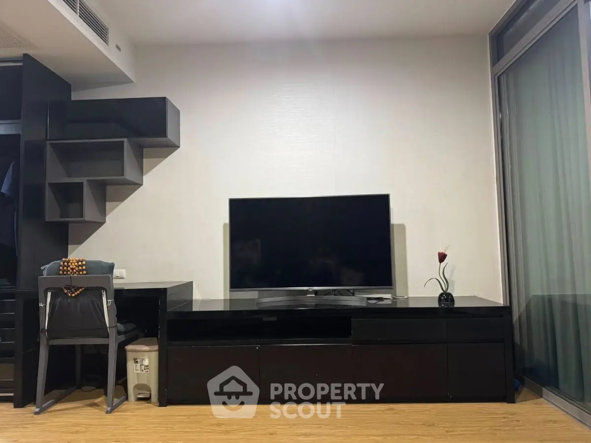 Modern living room with sleek black furniture and large TV, featuring a stylish wall shelf and wooden flooring.