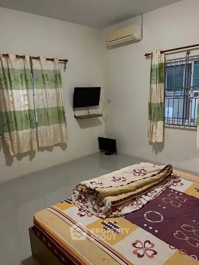 Cozy bedroom with air conditioning and wall-mounted TV, featuring floral curtains and a comfortable bed.