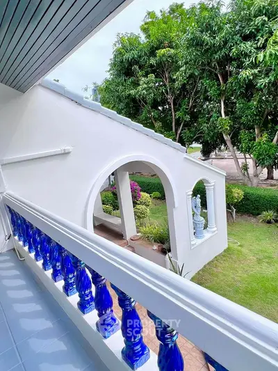 Charming balcony with vibrant blue railing overlooking lush garden and elegant archway