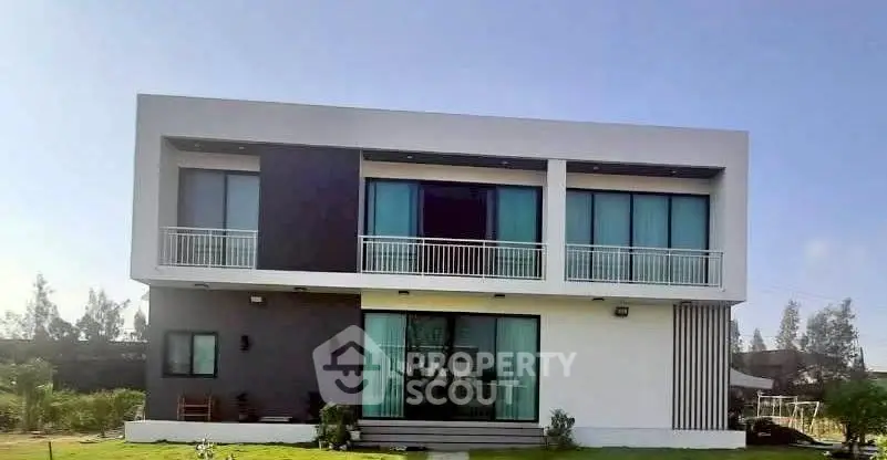 Modern two-story house with sleek design and large windows, surrounded by lush greenery.