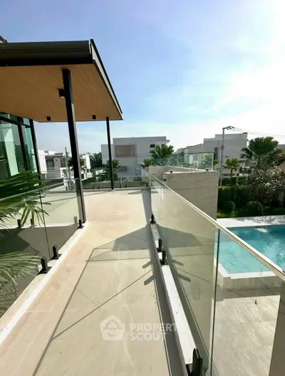 Luxurious modern balcony with glass railing overlooking pool and garden in upscale neighborhood.