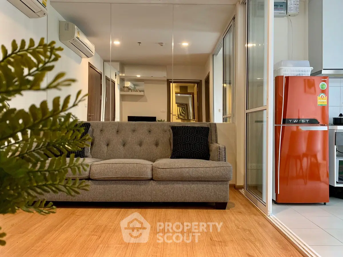 Modern living room with stylish sofa and vibrant red fridge, featuring wooden flooring and mirrored wall.