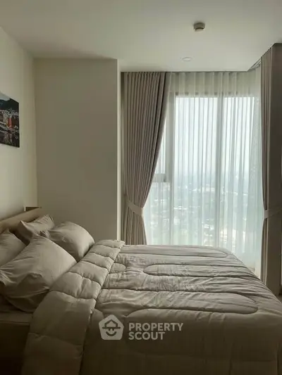 Cozy bedroom with large window and elegant curtains offering natural light and city view.