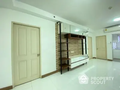 Spacious and well-lit living room with glossy white tiles, elegant brick accent wall, and built-in shelving units, perfect for modern living.