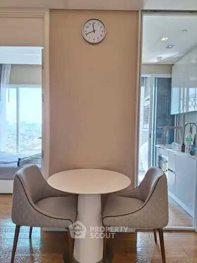 Modern apartment interior with dining area and kitchen view, featuring stylish chairs and a cityscape backdrop.