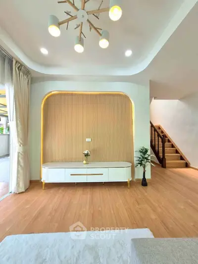 Modern living room with stylish lighting and wooden flooring, featuring a sleek media console and elegant staircase.