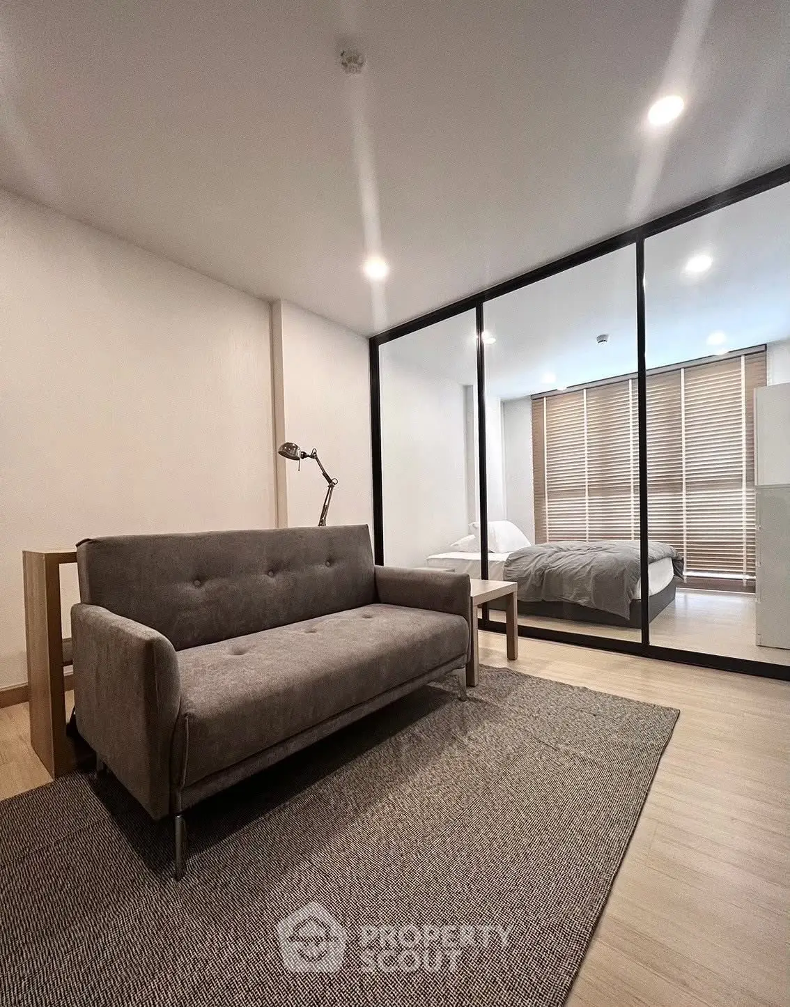 Modern studio apartment with glass partition, cozy sofa, and stylish bedroom.